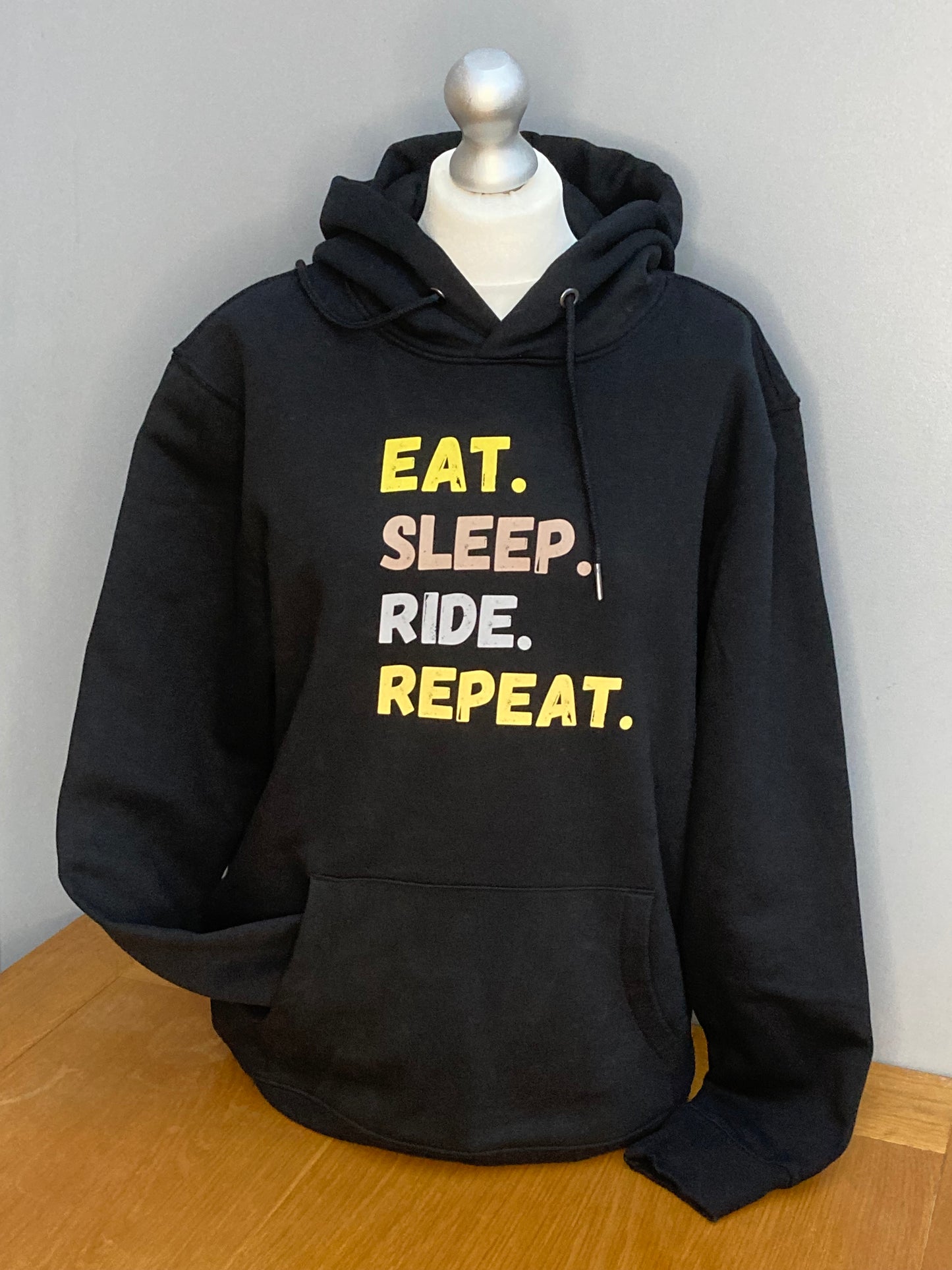 Black hoodie with front pocket showing a printed design in vibrant colourful print saying Eat, Sleep, Ride, Repeat.