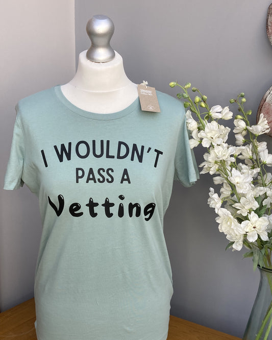 A green ladies fit T-shirt with the text 'I WOULDN'T PASS A VETTING' printed in bold lettering on the front, displayed on a mannequin.