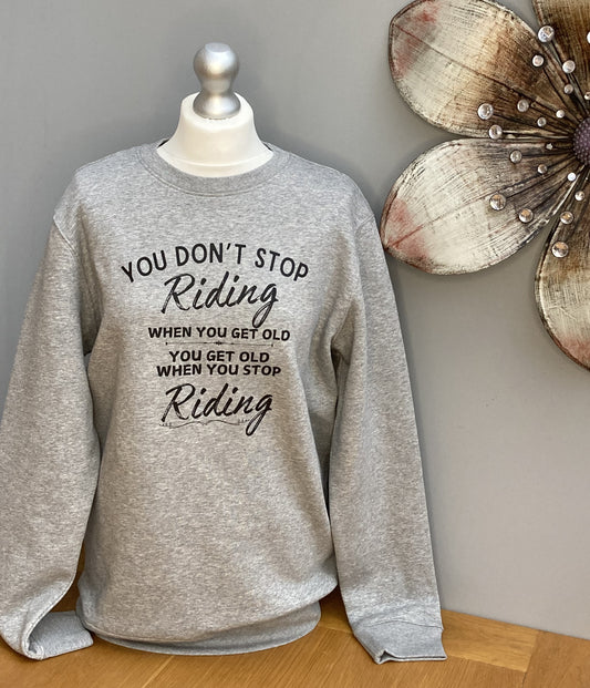 grey crew neck sweatshirt with the words printed on the front "You don't stop riding when you get old, you get old when you stop riding"
