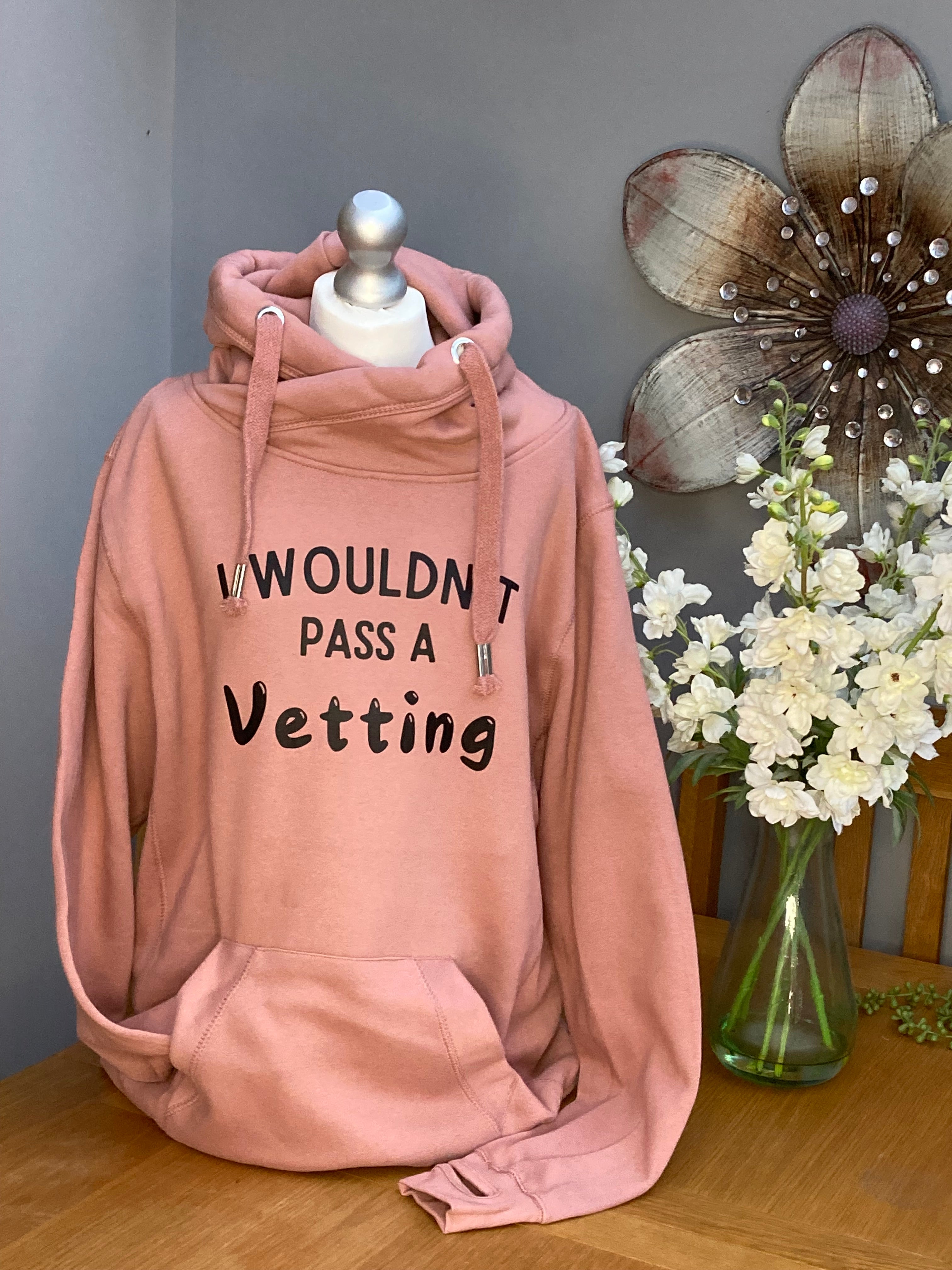 A pink cross neck hood with hood and front pocket and slogan printed on the front saying I wouldn't pass a vetting 